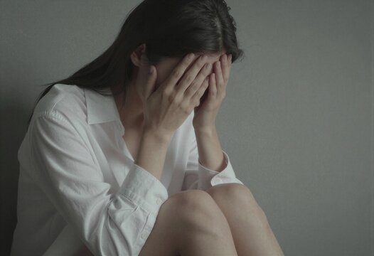 Una mujer sentada en el suelo, con la cara oculta entre las manos, transmitiendo una profunda tristeza y vulnerabilidad.
