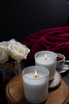 Warm candlelight beside a cup of tea, red roses, and a soft blanket creates a cozy romantic self-care setting. This intimate scene evokes relaxation, mindfulness, and quiet moments, perfect for Valent