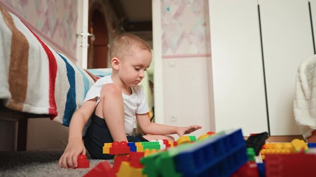 Young boy arranging bright blocks. Little boy concentrates on assembling vibrant plastic bricks nearby. Young child engaging in educational play by stacking multicolored building blocks on carpet