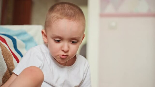 White boy focused on building with blocks on floor, intent expression as he examines shapes and stacks pieces in calm bedroom setting closeup of concentration and fine motor play.