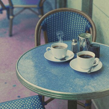 Una escena tranquila de dos tazas de caf&eacute; humeantes sobre una mesa azul en un caf&eacute; al aire libre.