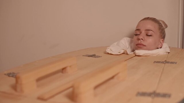 Young woman relaxing in wooden sauna phyto barrel at spa, enjoying wellness treatment, detox and body care concept