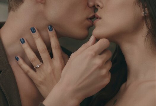 Primer plano de dos personas bes&aacute;ndose, con un anillo de compromiso visible.
