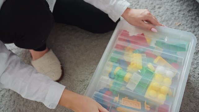 Parent organizes play items. Mother carefully arranges toys. Woman systematically sorts colorful toy parts. Parent and caregiver methodically organize and store vibrant toy pieces after playtime