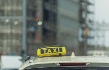 Fototapeta premium Yellow taxi sign atop a vehicle. City background blurred, urban setting. Ideal for transportation, travel, or urban life themes