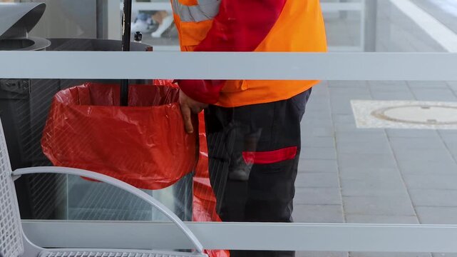Municipal sanitation worker replacing a trash bag in a public street bin at the train station. Urban cleaning and waste management scene 
