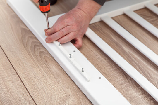 Process of assembling a baby cot. Soft focus. Man screws the side part with a screwdriver