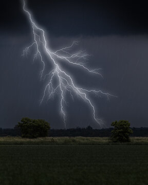 Lightning strike over farm field with trees under dark rain clouds
