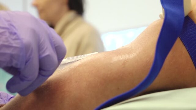 Close-up of arm with medical needle insertion during blood donation process in a clinical setting with healthcare professional present