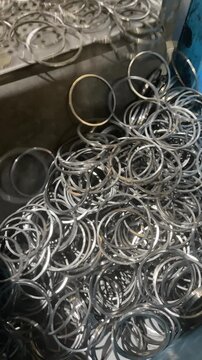 Steel rings falling into a box during a vibrating process, manufacturing of steel rings, close up of a blue industrial container filled with many shiny circular metal rings or gaskets in a