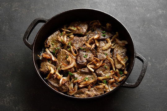 Sauteed liver with butter and onion in pan on black stone background