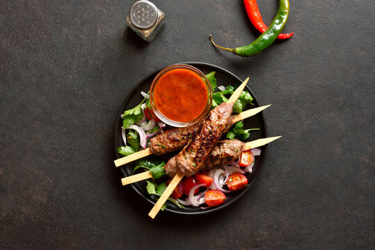Grilled lula kebab on skewers served with fresh vegetables and sauce