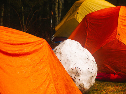 colorful tents wet from snow surround a large snowball in the morning at a winter campground
