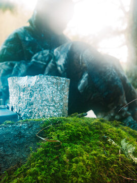 Shrouded in steam and fog, a young man heats water on a compact canister stove while camping in winter.