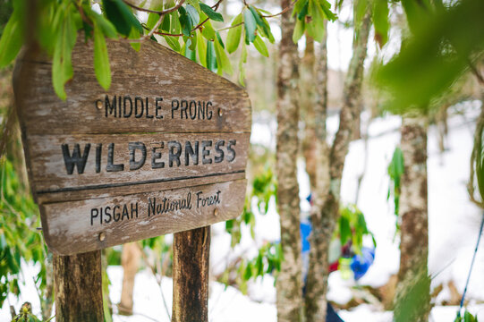 Backpackers pass an aged wooden sign along a trail in winter