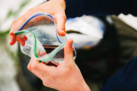 Hands open a plastic bag containing strips of beef jerky while winter camping