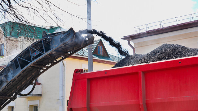 Asphalt milling machine loading recycled pavement into a red dump truck