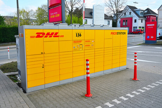 ISERLOHN, GERMANY - MARCH 27, 2026: A yellow DHL Packstation 136 automated parcel locker located near a Penny supermarket