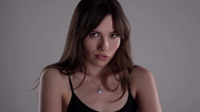 Confidence and self-esteem A young woman looks directly at the camera in a studio setting with a neutral background captured in slow motion commercial or editorial projects The clip conveys beauty.