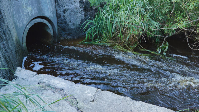Polluted wastewater discharging from a concrete pipe into a dark turbulent river