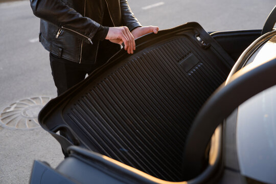 Hands placing protective rubber mat into car trunk, closeup of luggage compartment during organization and cargo protection.