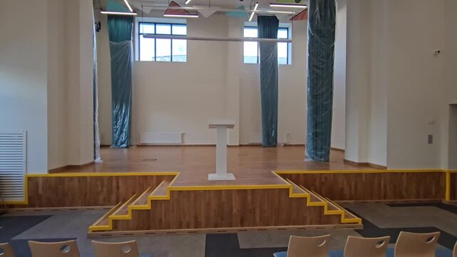 Large auditorium with rows of chairs and a podium. The chairs are empty and the room is mostly empty