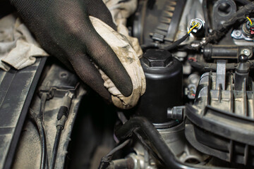 Gloved hand cleaning oil filter housing with cloth, closeup of wiping surface during car engine...