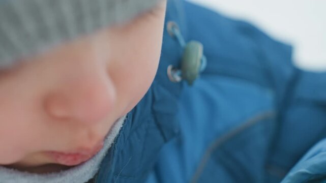 Toddler concentrates blowing bubble ring on snowy playground, closeup of lips and wand, blue winter coat and knit hat, delicate iridescent film forming, calm focused mood capturing practice and small