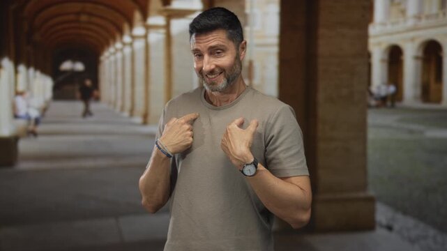 Man points thumbs to chest in building arcade with bracelets and watch visible; awkwardness self reference.