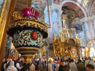 Fototapeta premium Large crowd of people are gathered in a church, with a large gold and blue candle holder hanging from the ceiling. The candle holder is lit, and the people are standing around it