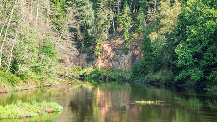 Obraz premium Calm river reflecting a forest and sandstone cliff