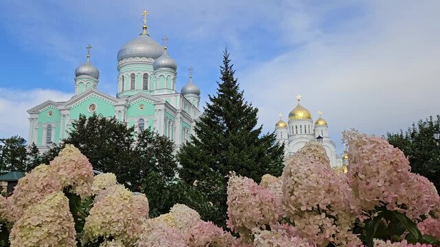 Church with a large green dome and a tree in front of it. The tree is surrounded by pink flowers