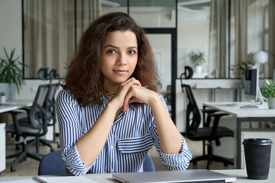 Young latin hispanic teen girl college student or intern sitting at table with laptop in campus looking at camera. University online classes, distance study, remote virtual learning concept, portrait
