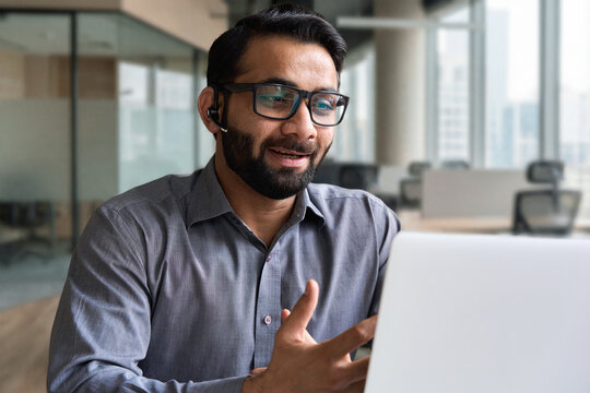 Indian business man speaking having virtual meeting on laptop. Professional remote online customer service support manager wearing headset talking consulting on video call at home office call center.