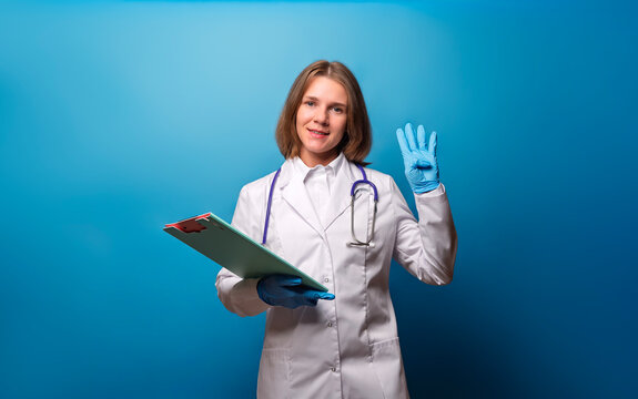 The female doctor shows the number 4 four. Doctor in white coat and blue gloves showing four fingers and holding a clipboard.