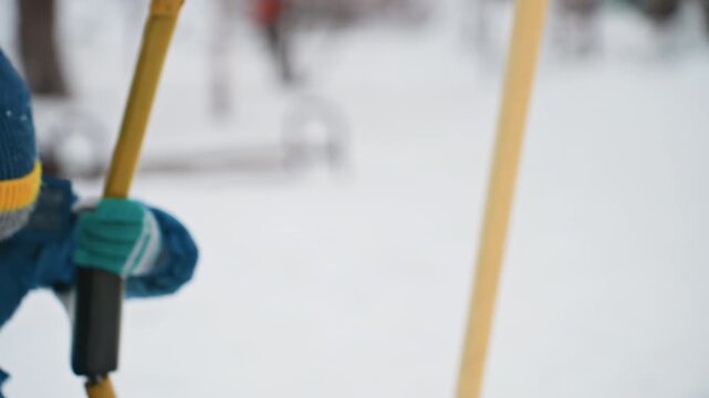 Closeup winter son on swing pensive portrait, bundled toddler in blue coat and knit hat grips yellow swing straps, soft falling snow and blurred park background, quiet reflective mood