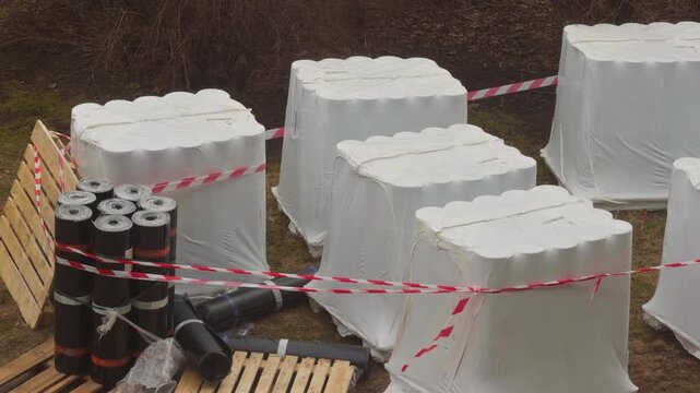 Hazard tape surrounds staged materials on outdoor construction area under overcast skies