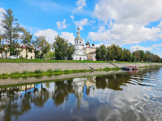 Fototapeta premium Church is in the background of a city with a river in the foreground. The water is calm and the reflection of the church can be seen in the water
