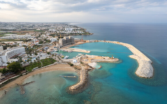 Paralimni, Protaras, Ayia triada marina development featuring luxury buildings, breakwaters, and a beach, with the town and mediterranean sea