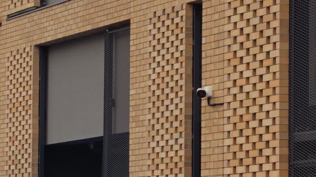 Security camera surveilling patterned brick structure under cloudy sky