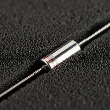 Close up of a resistor with a silver body and colored bands on a textured black foam surface.