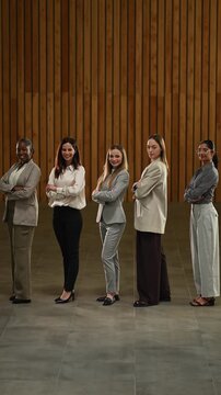 Diverse group of confident businesswomen standing in a row with arms crossed looking at the camera and smiling in an office