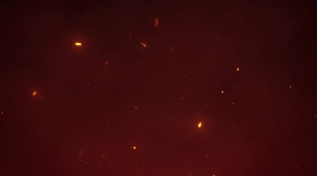 Cinematic red background with glowing fire embers and flying sparks. Abstract heat and burning particles effect for video overlay.