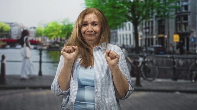 Woman holding both hands in a nervous airquote gesture while standing on a cobbled city street beside a canal bridge; uncertainty apology.