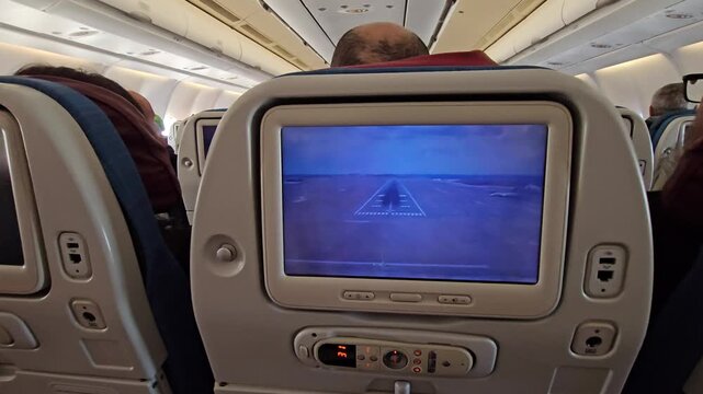 Man is sitting in an airplane with a screen in front of him. The screen is showing a video of a runway in airplane