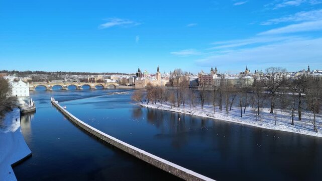 Aerial view of snowy Prague, Czech Republic. Winter cityscape with Snow-covered rooftops, Vltava River, and sunny blue sky