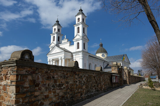 A stone fence along the Roman Catholic Cathedral. A grand white temple with two bell towers. A religious building in a provincial town.
