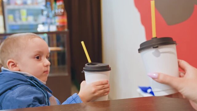 Warm cafe scene with mother and son enjoying drink. Mother and child share tender moment over drinks at cafe. Cozy cafe moment capturing mother and son bonding over refreshing drink together