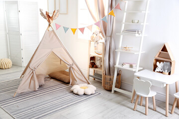 Stylish toy wigwam, furniture, pillows and decor in light playroom. Interior design © New Africa