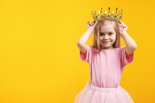 Beautiful little girl with crown dreaming about becoming queen on orange background, space for text